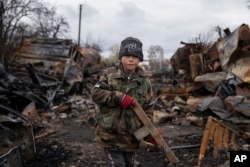 Yehor, 7, stands holding a wooden toy rifle next to destroyed Russian military vehicles near Chernihiv, Ukraine, Sunday, April 17, 2022. Witnesses said multiple explosions believed to be caused by missiles struck the western Ukrainian city of Lviv early Monday as the country was bracing for an all-out Russian assault in the east. (AP Photo/Evgeniy Maloletka)