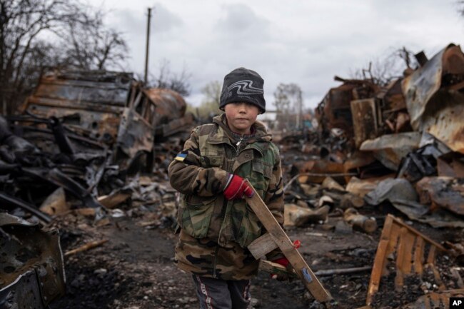 Yehor, 7, stands holding a wooden toy rifle next to destroyed Russian military vehicles near Chernihiv, Ukraine, Sunday, April 17, 2022. Witnesses said multiple explosions believed to be caused by missiles struck the western Ukrainian city of Lviv early Monday as the country was bracing for an all-out Russian assault in the east. (AP Photo/Evgeniy Maloletka)