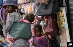 FILE - A woman with two children walks through the busy Bara Taxi Rank in Soweto, South Africa, April 5, 2022.