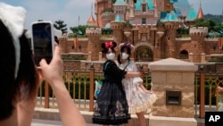Para pengunjung Disneyland Hong Kong berfoto sambil mengenakan masker ketika berkunjung ke taman wisata populer tersebut pada 21 April 2022. (Foto: AP/Kin Cheung)
