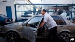 FILE - Taxi driver Michael Villegas pushes his car to keep his place in a line of drivers waiting to buy new car batteries in Caracas, Venezuela, Aug. 6, 2015. Drivers faced a gasoline shortage a week ago in the South American OPEC nation.