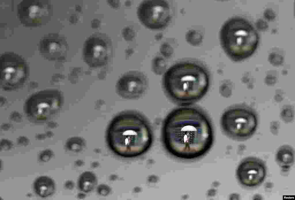 A man walking past a stock index board is reflected in the rain drops on a car window in Tokyo, Japan.