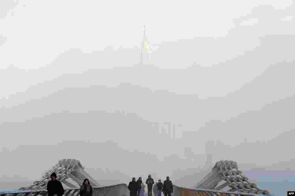 Pedestrians cross the Millennium Footbridge in front of London&#39;s St. Paul&#39;s Cathedral, shrouded in fog.