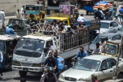 FILE - People ride on the back of a mini truck after the government resumed public transport services easing the lockdown imposed against the spread of the coronavirus, in Pakistan's port city of Karachi, June 3, 2020.