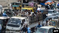 People ride on the back of a mini truck after the government resumed public transport services easing the lockdown imposed against the COVID-19 coronavirus, in Pakistan's port city of Karachi, June 3, 2020. 
