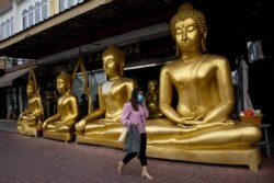 Seorang perempuan mengenakan masker, saat berjalan melewati patung Buddha emas di Bangkok, 5 Januari 2021, setelah pemerintah Thailand memberlakukan pembatasan wilayah akibat pandemi Covid-19. (Foto: Jack TAYLOR / AFP)