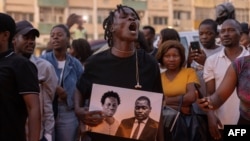 A man reacts as he holds an image of Paulo Guambe,left, and Elvino Dias, both associated with Mozambique's opposition party PODEMOS, during a vigil the day after they were shot dead in Maputo, Mozambique, Oct. 19, 2024.