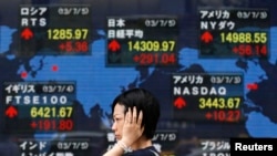 FILE - A woman walks past an electronic board displaying Japan's Nikkei average (top C) and various countries' stock price indices outside a brokerage in Tokyo.