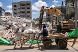 FILE - A horse-drawn cart passes a worker using an excavator to dig through debris of a building destroyed by an airstrike prior to the cease-fire in Gaza City, May 22, 2021.
