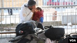 A man and child try to keep warm as they wait at the migrant and refugee registration center in Presevo, Serbia, Jan. 19, 2016. (P. Walter Wellman/VOA)