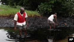 FILE - Men walk in an oil slick covering a creek near Bodo City in the oil-rich Niger Delta region of Nigeria, June 20, 2010.