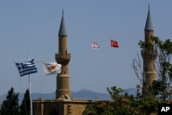 (From left to right) Greek and Cyprus' flags, a Turkish and Turkish Cypriot breakaway flags fly on a minaret of the Selimiye mosque, or Cathedral of St Sophia in divided capital Nicosia, Cyprus, April 26, 2021.