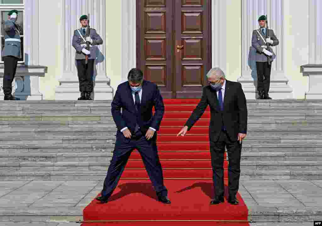 Wearing face masks to protect agains the coronavirus, German President Frank-Walter Steinmeier, right, shows Croatia&#39;s President Zoran Milanovic where to stand during a welcome ceremony at the Bellevue Palace in Berlin, Germany.