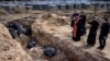 Priests pray at a mass grave in the garden surrounding the St. Andrew church in Bucha, Ukraine, on April 7, 2022. (RONALDO SCHEMIDT/AFP)