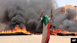 A protester wearing a Sudanese flag flashes the victory sign in front of burning tires and debris on Road 60, near Khartoum's army headquarters, in Khartoum, Sudan, June 3, 2019.