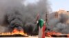 A protester wearing a Sudanese flag flashes the victory sign in front of burning tires and debris on road 60, near Khartoum's army headquarters, in Khartoum, Sudan, Monday, June 3, 2019.