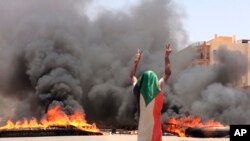 FILE - A protester wearing a Sudanese flag flashes the victory sign in front of burning tires and debris on road 60, near Khartoum's army headquarters, in Khartoum, Sudan, June 3, 2019.