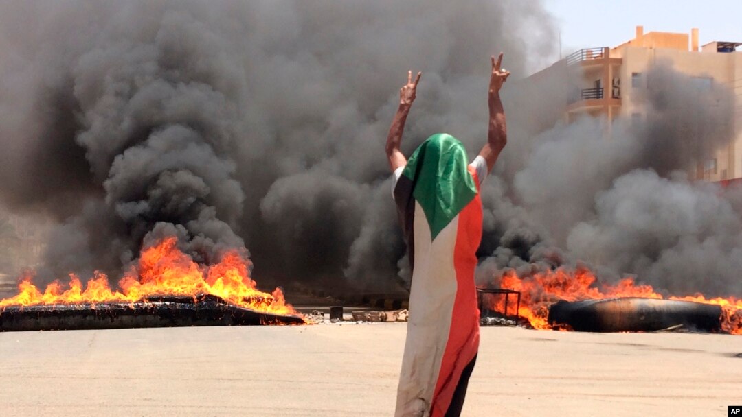Pengunjuk rasa mengenakan bendera Sudan berpose dengan tanda kemenangan di dekat kantor pusat tentara di Khartoum, Sudan.