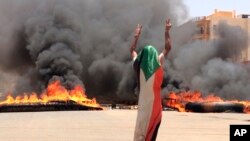 Pengunjuk rasa mengenakan bendera Sudan berpose dengan tanda kemenangan di dekat kantor pusat tentara di Khartoum, Sudan.