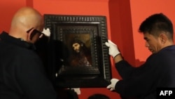 People hang a paining entitled "Study of the head and clasped hands of a young man as Christ in prayer," oil on oak panel, by Dutch painter Rembrandt on display at the Louvre Abu Dhabi, in the Emirati capital, Feb. 9, 2019.