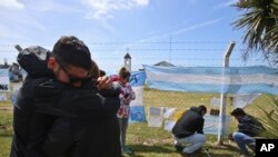 Kerabat dan teman Alejandro Tagliaprieta, salah seorang awak kapal selam ARA San Juan yang hilang, berpelukan di pangkalan Angkatan Laut. Warga menggantungkan bendera-bendera dan pesan-pesan di Mar de Plata, Argentina, 24 November 2017.