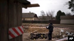 PAMJE TË RËNDA - Një oficer policie qëndron pranë gjashtë trupave të djegur, të paidentifikuar, të gjetur në tokë pranë një zone të banuar në Bucha, Ukrainë (5 prill 2022)