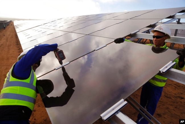 FILE - Workers install a solar panel at a photovoltaic solar park situated on the outskirts of the coastal town of Lamberts Bay, South Africa, March. 29, 2016. (AP Photo/Schalk van Zuydam, File)