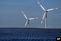 FILE - Wind turbines turn behind a solar farm in Rapshagen, Germany, Oct. 28, 2021.