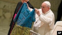 Pope Francis shows a flag that was brought to him from Bucha, Ukraine, during his weekly general audience in the Paul VI Hall, at the Vatican, Apr. 6, 2022. 