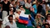 Seorang penonton yang memegang bendera Rusia menyaksikan pertandingan babak ketiga tunggal putra antara Daniil Medvedev dari Rusia melawan Marin Cilic dari Kroasia di Kejuaraan Tenis Wimbledon di London, 3 Juli 2021. (Foto: AP)