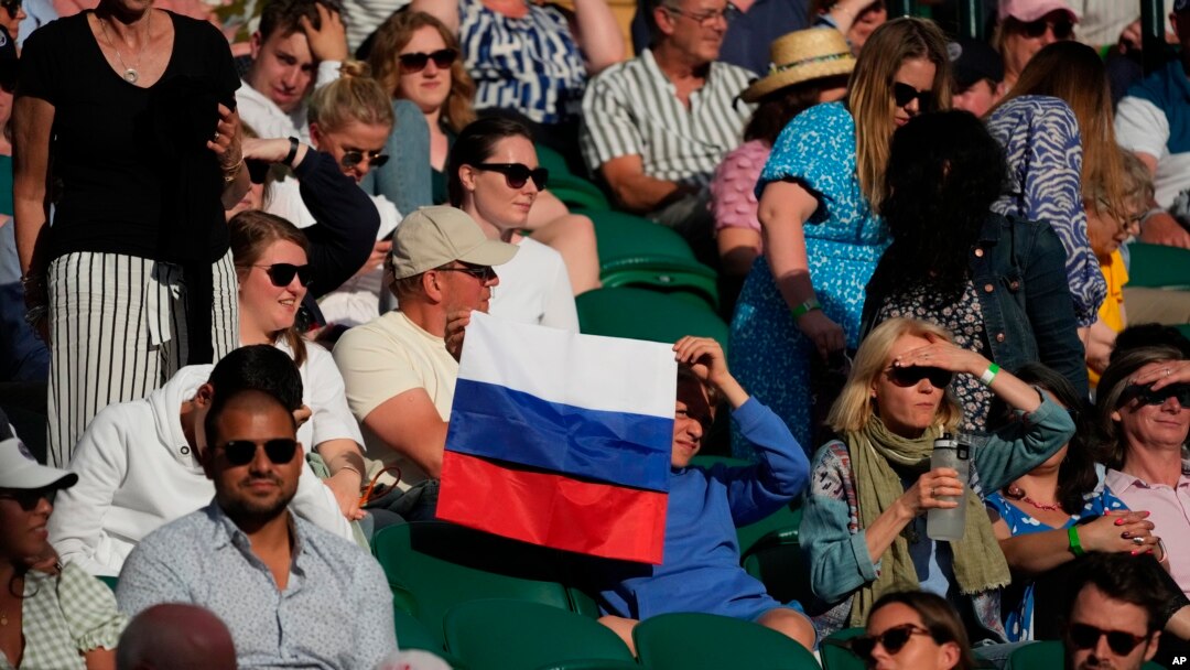 Seorang penonton yang memegang bendera Rusia menyaksikan pertandingan babak ketiga tunggal putra antara Daniil Medvedev dari Rusia melawan Marin Cilic dari Kroasia di Kejuaraan Tenis Wimbledon di London, 3 Juli 2021. (Foto: AP)