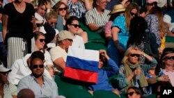 Seorang penonton yang memegang bendera Rusia menyaksikan pertandingan babak ketiga tunggal putra antara Daniil Medvedev dari Rusia melawan Marin Cilic dari Kroasia di Kejuaraan Tenis Wimbledon di London, 3 Juli 2021. (Foto: AP)