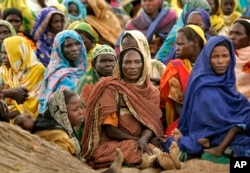 FILE - Women sit under the shade of a large tree on a wadi (dry riverbed) at a makeshift camp for internally displaced people near Seleah village, West Darfur, Sudan, Sept. 27, 2004.