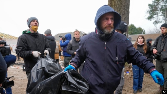 Policët mbartin kufomën e një civili të gjendur në Bucha (5 prill 2022)