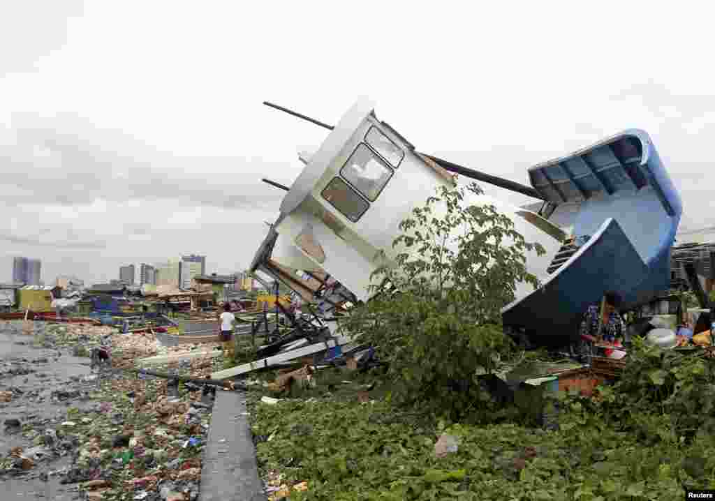 People walk near a boat destroyed by Typhoon Rammasun which battered the coastal bay of Baseco compound, metro Manila, July 16, 2014.