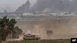 Sebuah tank angkatan darat Israel sedang melaju di perbatasan Jalur Gaza di selatan Israel, Sabtu 23 Desember 2023. Asap dari pengeboman Israel tampak membubung dari kejauhan. (Foto: Tsafrir Abayov/AP Photo)