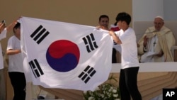 Jóvenes peregrinos de Corea del Sur celebran con su bandera nacional y con el Papa Francisco después de que anunció que la próxima Jornada Mundial de la Juventud será en Seúl, Corea del Sur, en 2027, luego de una misa en el Parque Tejo en Lisboa, el domingo 6 de agosto de 2023 .