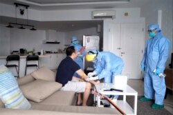 In this image from video taken March 27, 2020, an Indonesian local health service personnel draws blood from an individual on self-quarantine, in Jakarta, Indonesia.