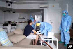 In this image from video taken March 27, 2020, an Indonesian local health service personnel draws blood from an individual on self-quarantine, in Jakarta, Indonesia.