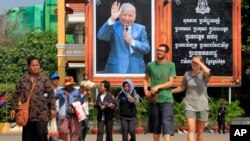 Foreign tourists, right, walk in front of Cambodia's late King Norodom Sihanouk portrait ahead of his funeral, Thursday, Jan. 31, 2013, in Phnom Penh, Cambodia. The body of Sihanouk who died on Oct. 15, 2012 at age 89, is scheduled to be cremated on Feb. 4, 2013. (AP Photo/Heng Sinith)