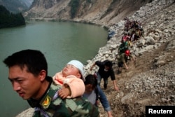 FILE - Survivor carries baby on his back as he and some 1,000 other survivors make a 9-hour walk from the village of Qingping to Hanwang, after earthquake, Sichuan Province, China, May 16, 2008.