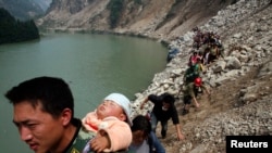 FILE - Survivor carries baby on his back as he and some 1,000 other survivors make a 9-hour walk from the village of Qingping to Hanwang, after earthquake, Sichuan Province, China, May 16, 2008.
