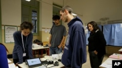 Carlo Andrea Carnevale Ricci, president of a voting section, checks the electronic voting operation system with a technician, left, at the Berchet School polling station, in Milan, Italy, Saturday, Oct. 21, 2017. It is greater autonomy, not independence,