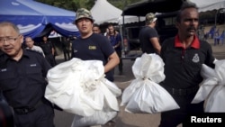 Forensic policemen carry body bags with human remains found at the site of human trafficking camps in the jungle close the Thailand border after they brought them to a police camp near Wang Kelian in northern Malaysia, May 25, 2015.