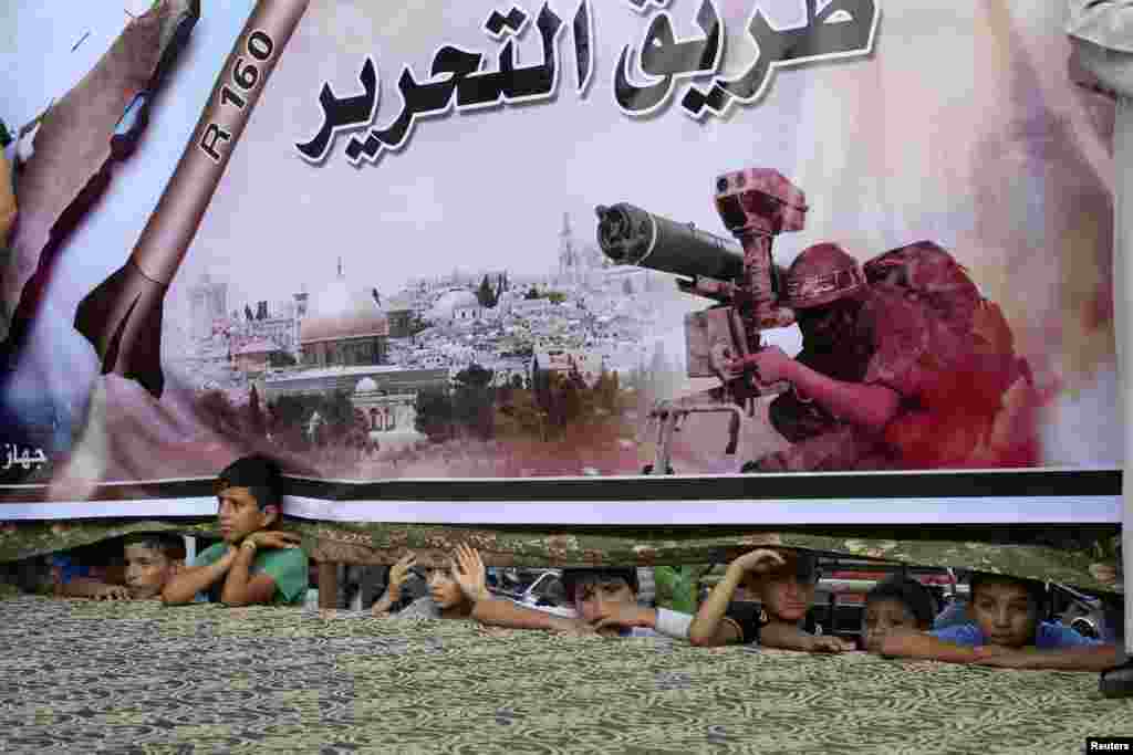 Palestinians watch through a large Hamas poster at a rally in support of the armed Palestinian factions, in Rafah in the southern Gaza Strip, Aug. 17, 2014.