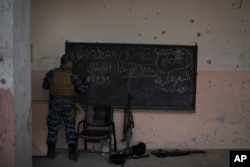 A Federal Police soldier writes in Arabic "Federal Police are heroes" on a black board in a school that they say was used by Islamic State militants in Mosul, Iraq, March 28, 2017.
