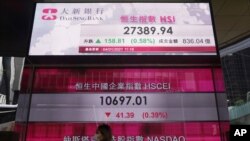 A woman walks past a bank's electronic board showing the Hong Kong share index at Hong Kong Stock Exchange, Jan. 4, 2021.