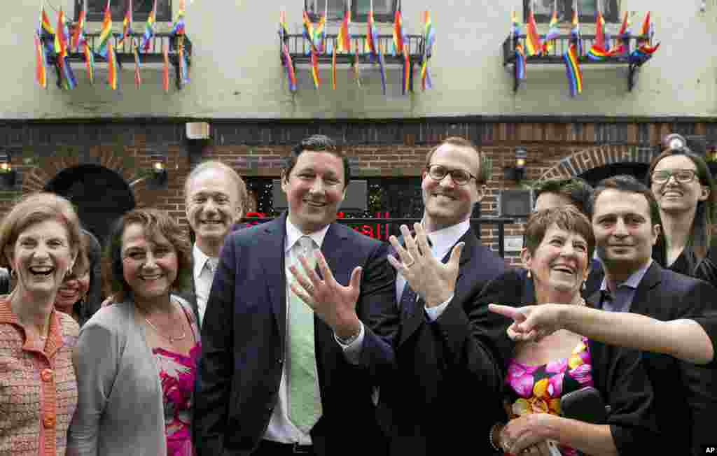 David Turley (tengah, kiri) dan suaminya Peter Thiede, memamerkan cincin kawin mereka saat berfoto bersama kawan dan keluarga (28/6) di Stonewall Inn, New York. Gubernur New York Andrew Cuomo sebelumnya menikahkan pasangan tersebut. (AP Photo/Mark Lennihan)