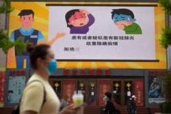People wear face masks to protect against the spread of the new coronavirus as they walk past a screen showing a video about criminal penalties for not cooperating with medical rules in Beijing, April 15, 2020.