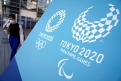 A woman walks near a sing of the Tokyo 2020 Olympic and Paralympic Games, Aug. 20, 2021, in Tokyo. The Tokyo Paralympics open on Aug. 24 in a ceremony at Tokyo's National Stadium.